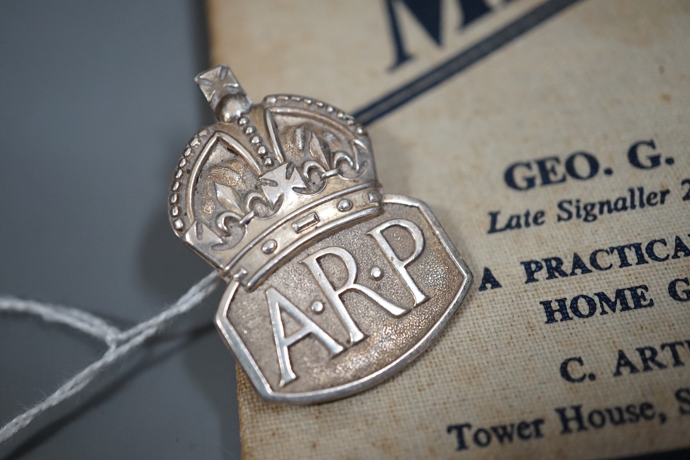 A silver Air Raid Precautions badge and Homeguard signalling manual